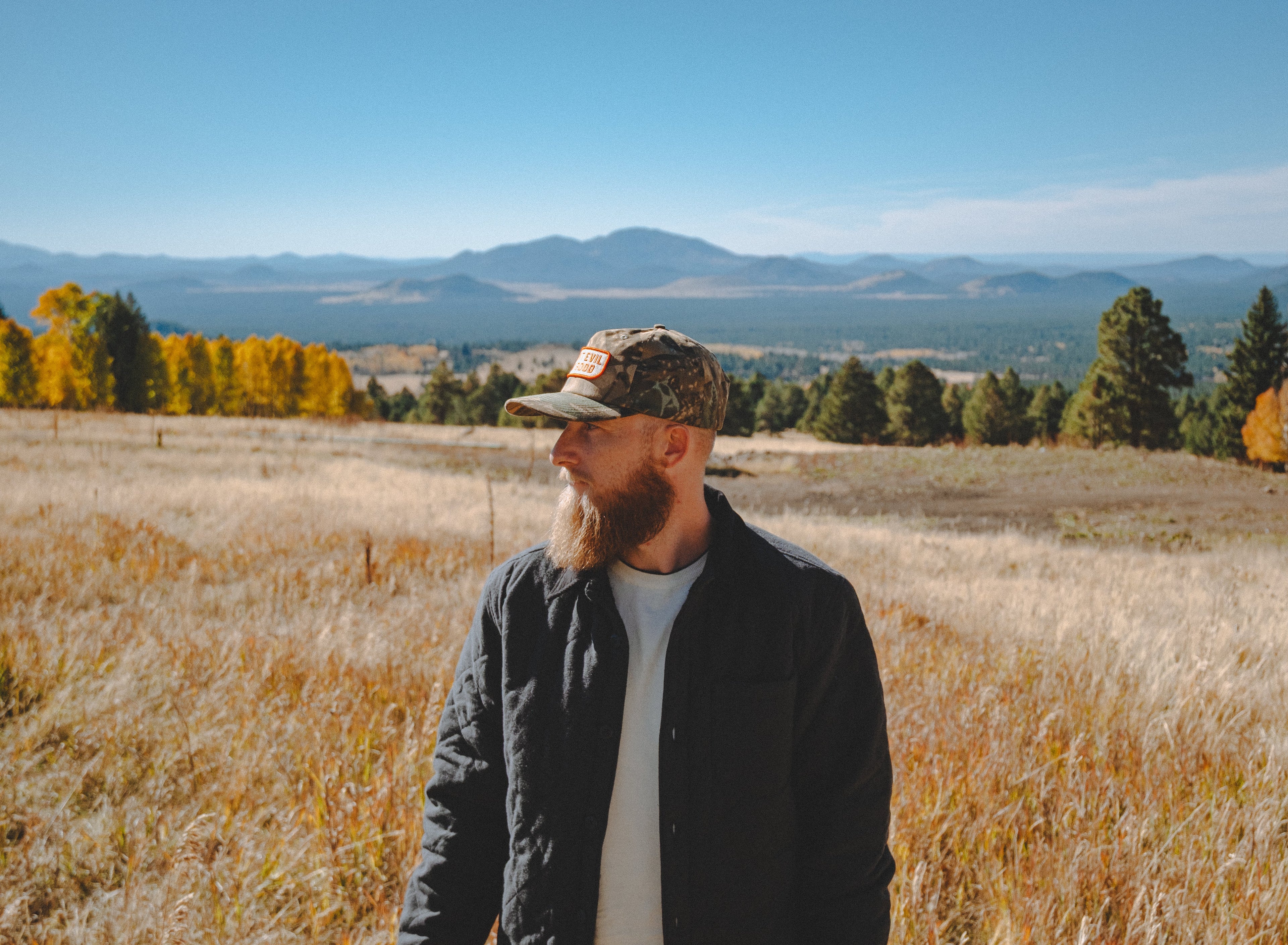 Man standing in a field with autumn trees and mountains in the background